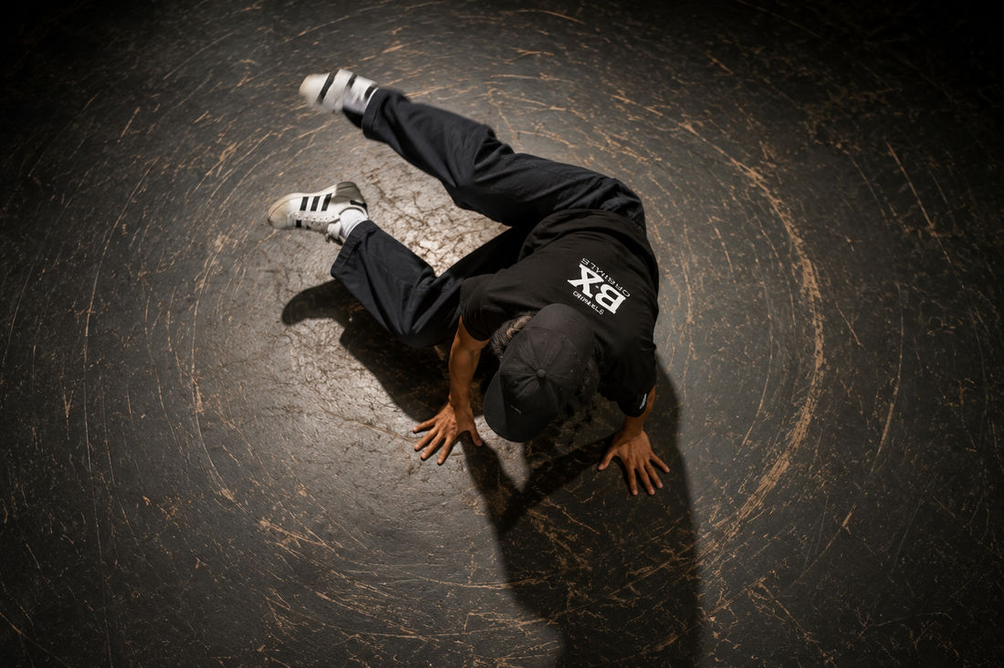 A breaker mid-footwork, shot from overhead — hands supporting the body while the legs trace a circular pattern.
