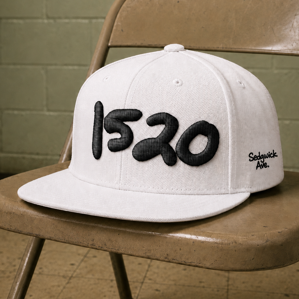 White 1520 Cap with black handstyle embroidery resting on a vintage chair