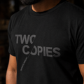 Close-up of the charcoal TWO COPIES print on the black tee